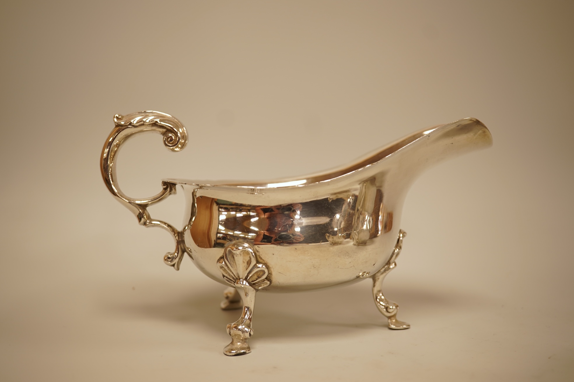 A pair of George V silver sauceboats by Walker & Hall, Sheffield, 1929/30, length 17.9cm together with a George V silver sauceboat with flying scroll handle, William Comyns & Sons Ltd, London 1926, 16.4oz.